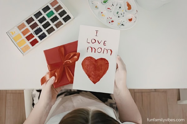 a kid holding a gift and card for her mother on mother's day