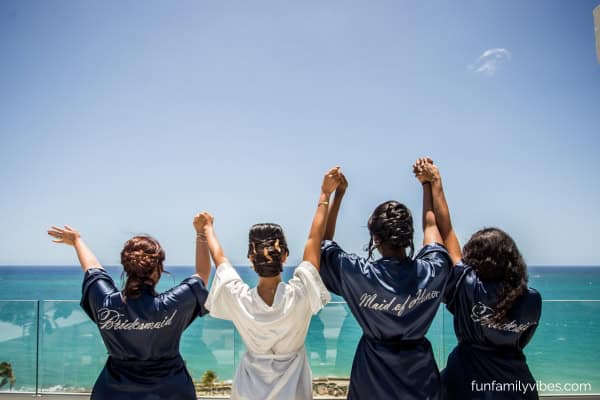 four women holding hands facing the ocean in a bachelorette party