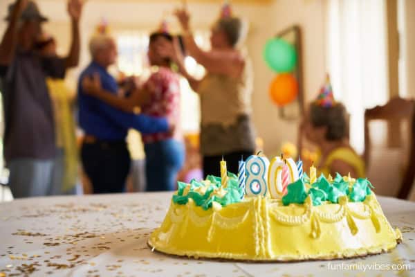 birthday cake with number '80' candles, people celebrating in the background