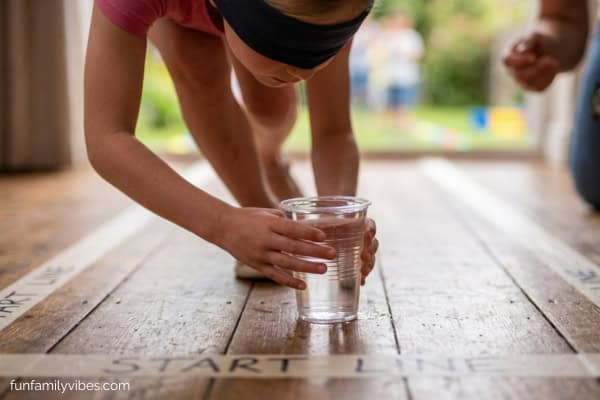 blindfolded girl setting down a plastic cup filled with water onto the floor.