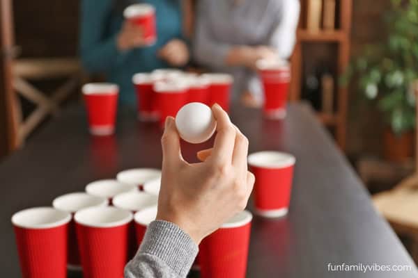 a hand holding a pingpong ball, red plastic cups on the table